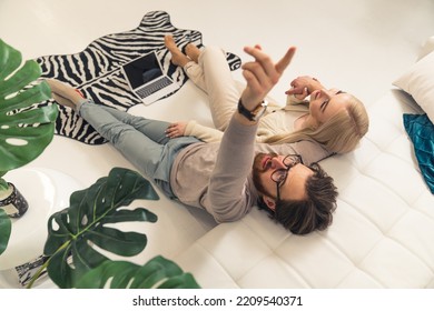 White Couple Sitting On The Floor By A Couch In Front Of A Laptop The Man Looking At The Ceiling And Pointing With Finger. Indoor Shot. High Quality Photo