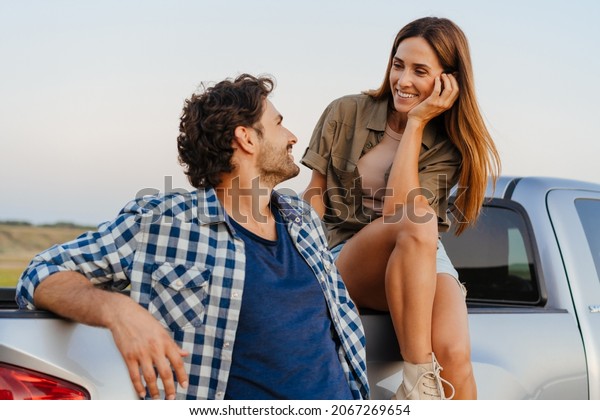 White couple smiling and talking while leaning\
on their car outdoors