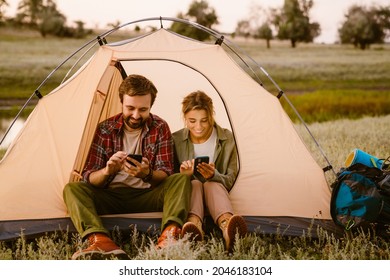 White Couple Using Cellphones And Sitting In Tent During Camping Together On Summer Day