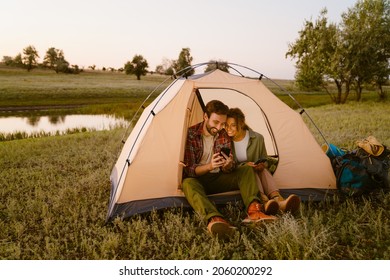 White couple using cellphones and sitting in tent during camping together on summer day - Shutterstock ID 2060200292