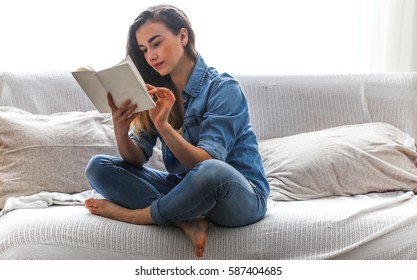 White cozy bed and a beautiful girl, reading a book, concepts of home and comfort, place for text