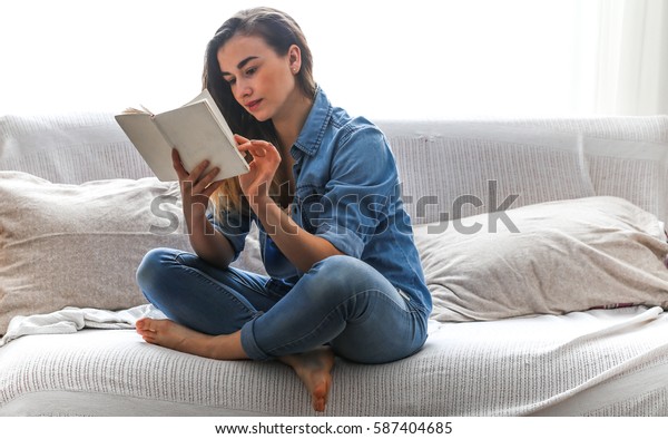 White cozy bed and a beautiful\
girl, reading a book, concepts of home and comfort, place for\
text