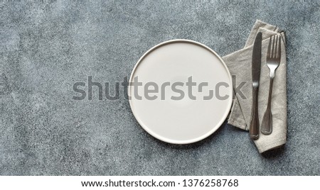 White craft plate, cutlery and napkin on white stone table. knife and fork on beige napkin. Top view, copy space. Table setting. background for menu, layout, recipe background, food flat lay