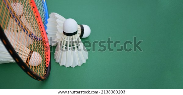 White\
cream badminton shuttlecocks, badminton rackets on green floor of\
indoor badminton court, soft and selective focus on shuttlecock,\
concept for badminton sport lovers around the\
world
