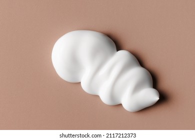 White cream texture. Cosmetic creamy product on brown background. Sunscreen, face creme, body lotion, hair conditioner swirl swatch closeup