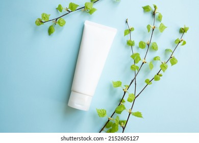 White Cream tube and birch branches with young small leaves on blue background. Cosmetic skincare product blank plastic package. White bottle of unbranded lotion, balsam, toothpaste mockup, flat lay.