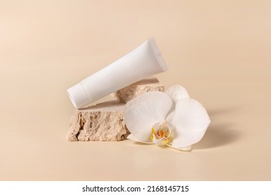 White cream tube on travertine stone near white orchid flower on light yellow, close up, mockup. Skincare handmade beauty product, cream or lotion. Exotic natural cosmetics