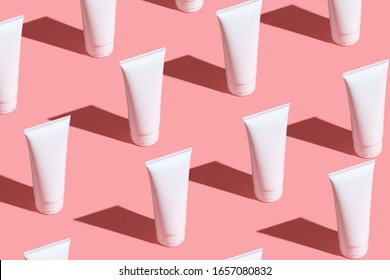 White Cream Tubes On Light Pink Table. Care About Face, Hands, Legs And Body Skin. Women Beauty Products. Cosmetic Pattern. Empty Place For Logo On Tubes. Hard Light Directly Flat Lay.