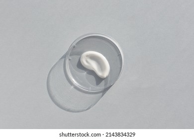 White creamy texture in a Petri dish on a gray background. Concept of cosmetics laboratory researches. Smear of skincare cosmetics product. Wellness and beauty concept. Soft focus