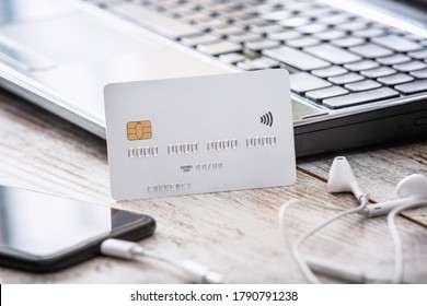 White Credit Or Debit Payment Card Mockup.Empty Banking Card On The Working Desk, Next To Mobile Phone And Laptop.