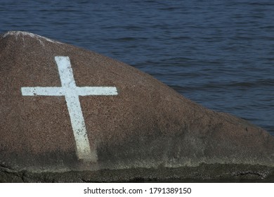 White cross painted on the rock in the sea. Close-up picture.