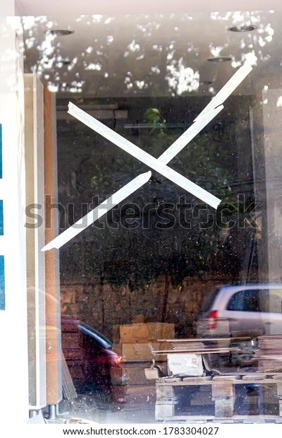 A white\
cross sign is on a dirty window of an empty shop at Inonu Street in\
Konak, Izmir, Turkey- July 16,\
2020