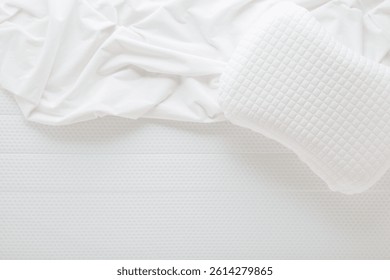 White crumpled bed sheet and memory foam pillow on soft mattress. Closeup. Top view.
