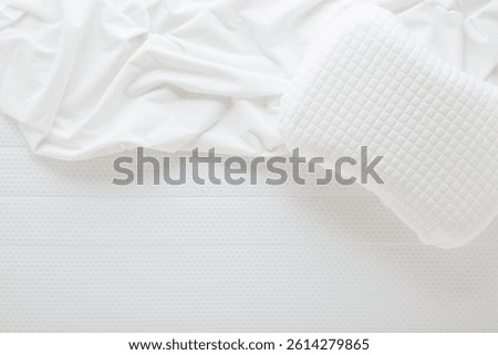 White crumpled bed sheet and memory foam pillow on soft mattress. Closeup. Top view.