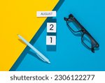White cube calendar with the date august 21 with stationery, or office accessories on a blue yellow background. Deadline, planning, business concept