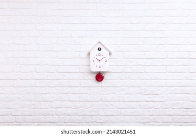 White Cuckoo Bird Clock With Red Round Pendulum And Dial On A White Brick Wall With Copy Space