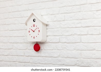 White Cuckoo Bird Clock With Red Round Pendulum And Dial On A White Brick Wall With Copy Space