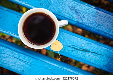 White Cup Of Black Tea Is On Old Blue Wooden Bench In Autumn Park.  Selective Focus With Shallow DOF, Top View