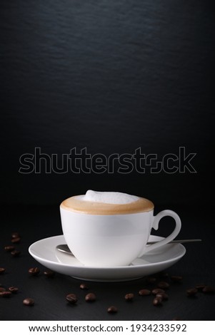 White cup of cappuccino on a black textured background. Italian cappuccino. Morning coffee in Italy. Coffee on black. Coffee beans. Close-up on a white cup.