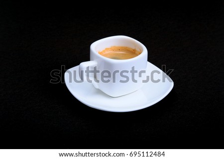 White cup of classic espresso coffee and pralines on black background.