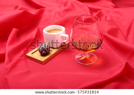 White cup of coffee and cognac in a glass, pralines on red background.