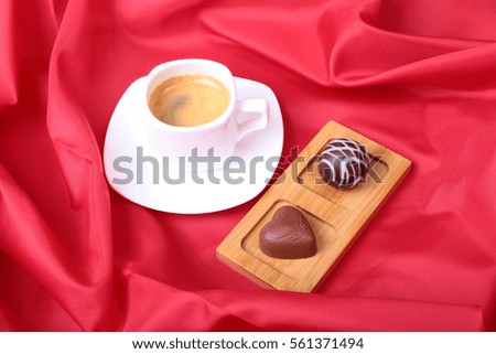 White cup of coffee and cognac in a glasses, pralines on red background.