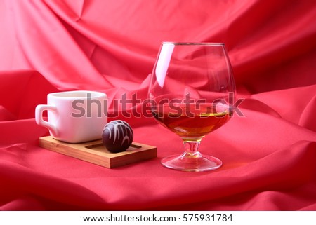 White cup of coffee and cognac in a glasses, pralines on red background.