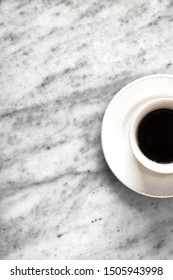 White Cup Of Coffee In The Left Corner Of The Frame On A Marble Carrara Table In A Vertical View