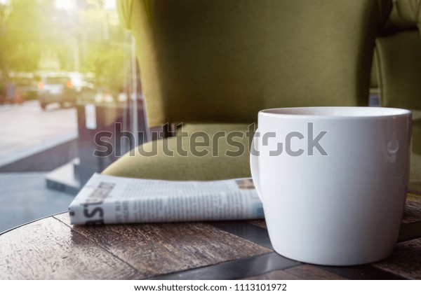White Cup of coffee with newspaper on the\
wooden table, street and car\
background.