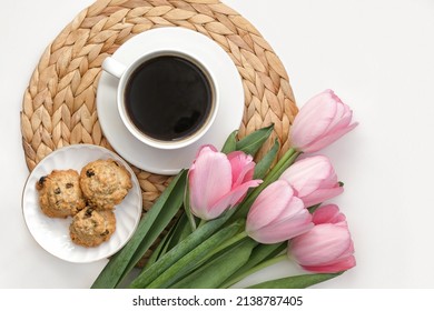White cup of coffee with pink tulips on white background. Morning coffee on wicker tray. View from above of morning coffee, cookies and flowers. Flat lay. Breakfast in bed. Stylish home interior decor