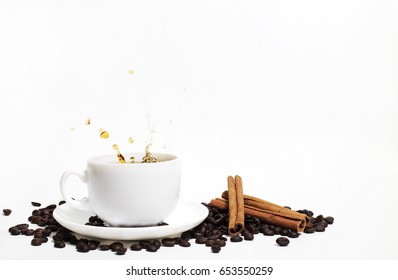 White cup of coffee with splash surrounded by coffee beans and cinnamon sticks.