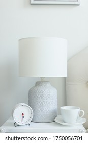 a white cup of coffee is standing on the bedside table, next to the lamp on which is a white lampshade