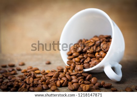 White cup with fair-trade coffee beans on wooden desk against warm blurry background