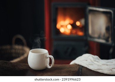 White cup with hot tea with burning fireplace on the background in cozy log cabin. - Powered by Shutterstock