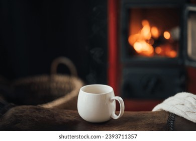 White cup with hot tea with burning fireplace on the background in cozy log cabin. - Powered by Shutterstock