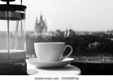 a white cup of hot tea and a teapot on the table, against the background of the city. Black and white photo