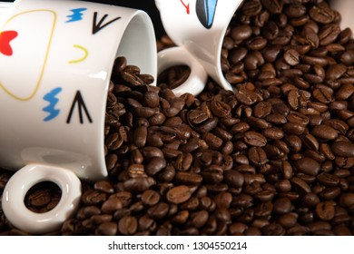 white cups with a pattern and grains of coffee on a black background