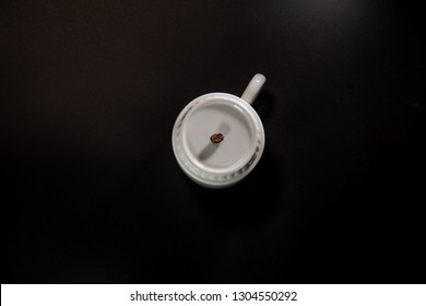 white cups with a pattern and grains of coffee on a black background
