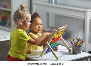 white and dark skinned children sit together at the table and count on the abacus and smiles
