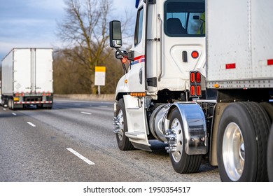 White day cab big rig industrial semi truck transporting commercial cargo in dry van semi trailer running in convoy behind another semi truck driving on the interstate highway road