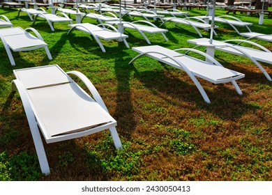 White deck chairs on the green grass at the hotel. Sun loungers on the lawn