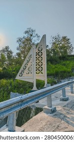 White decorative triangular monument standing beside a road barrier against clear blue sky.