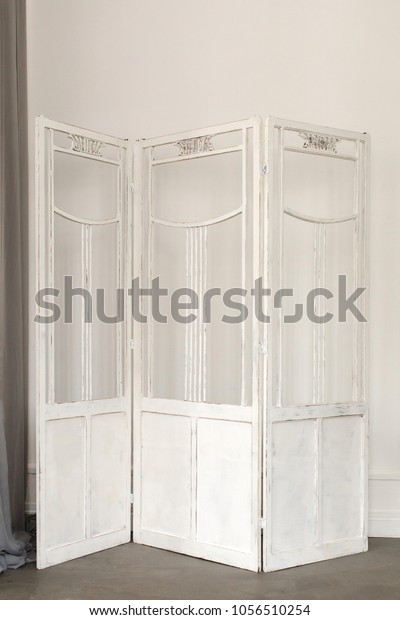 White delicate decorative wood panel on white\
plaster wall. Boudoir wedding room. Retro folding screen. Vintage\
ornate carved folding\
screen.