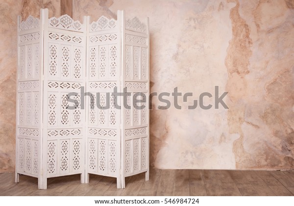 White delicate decorative wood panel on brown\
plaster wall. Boudoir wedding room. Retro folding screen. Vintage\
ornate carved folding screen.\
