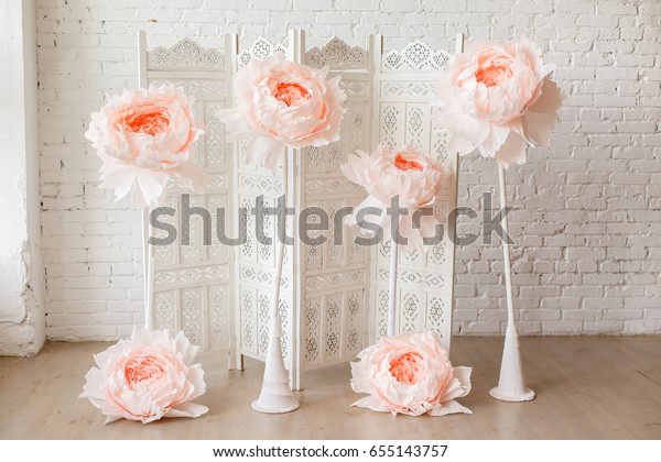 White delicate decorative\
wood panel with big paper flowers on white brick wall. Boudoir\
wedding room. Retro folding screen. Vintage ornate carved folding\
screen. 