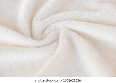 White Delicate Soft Background Of Plush Fabric Cozy Plaid. Texture Of Beige Soft Fleecy Blanket Textile With Twisted  Beautiful Folds.