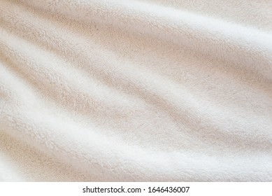 White Delicate Soft Background Of Plush Fabric Cozy Plaid. Texture Of Beige Soft Fleecy Blanket Textile With Twisted Beautiful Folds.