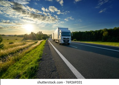 White Delivery Truck Driving On The Asphalt Road In Rural Landscape At Sunset