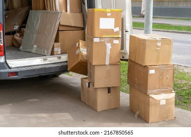 White Delivery Van And Many Different Cardboard Boxes At City Street. Open Lorry Car Trunk With Moving Cardboard Packages Outdoors.