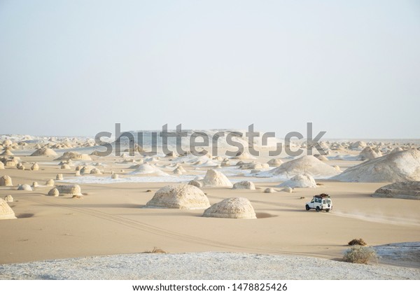 White desert bahariya egypt. White limestone rock\
formations and sand desert landscape. One off road car driving away\
on a trail. Scenic extreme nature background. Special travel\
destination. 